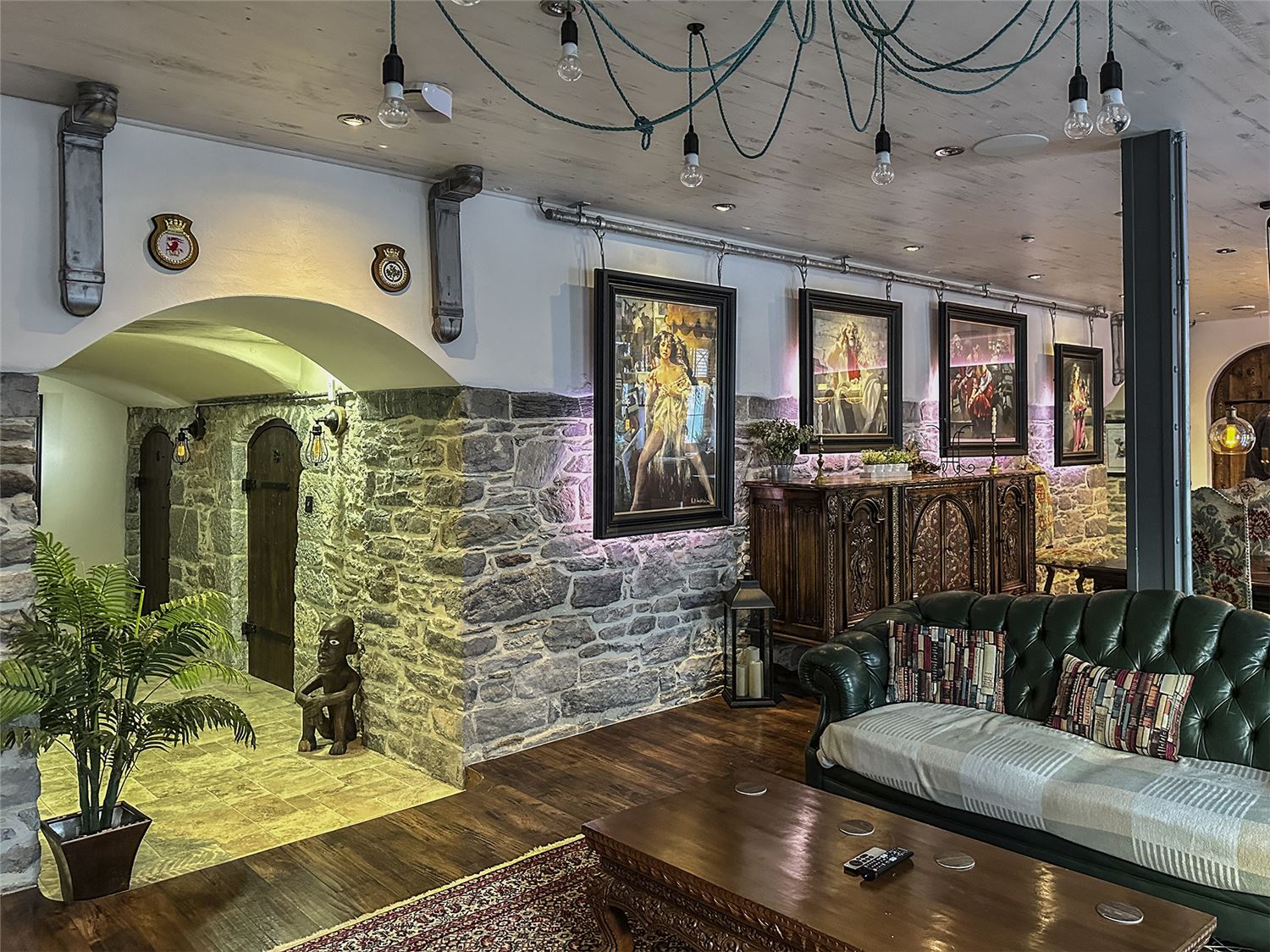 A view through the lounge towards the kitchen along the natural stone wall. A collection of pictures hang from the ceiling on an industrial rail